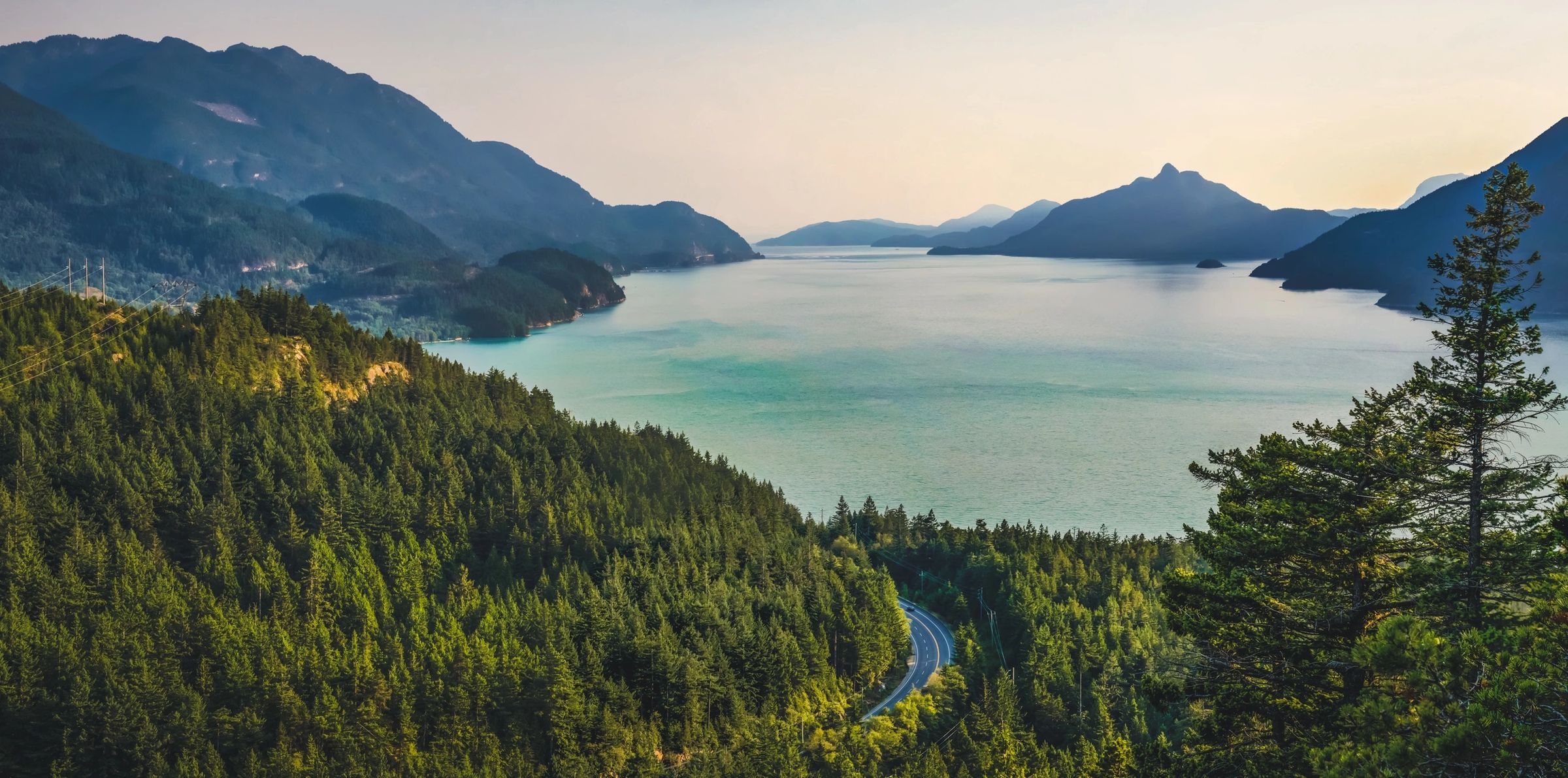 A blue lake surrounded by mountains. A road curves left at the bottom of the lake