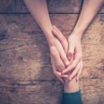 An adult holds hands with an anxious child over a wooden table