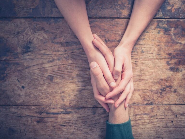 An adult holds hands with an anxious child over a wooden table